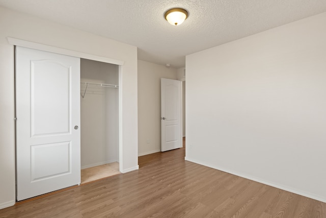 unfurnished bedroom with light wood finished floors, a textured ceiling, baseboards, and a closet