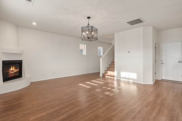 unfurnished living room featuring a large fireplace, baseboards, visible vents, wood finished floors, and stairs