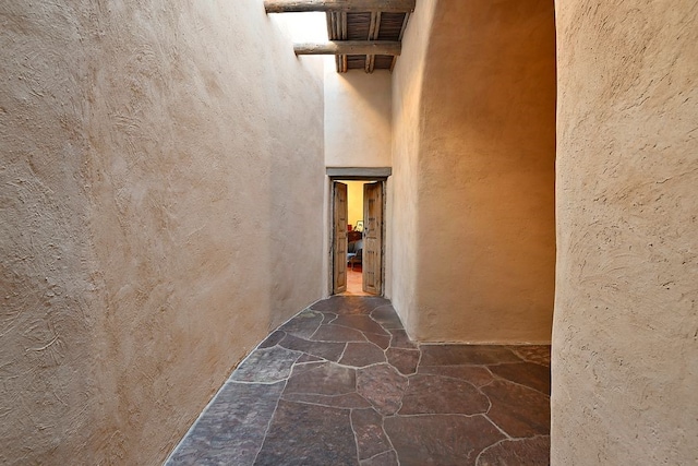 corridor with stone floors, visible vents, a textured wall, and a towering ceiling