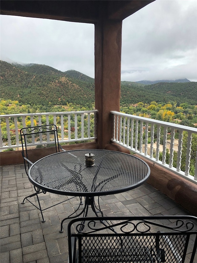 balcony featuring outdoor dining area, a mountain view, and a wooded view