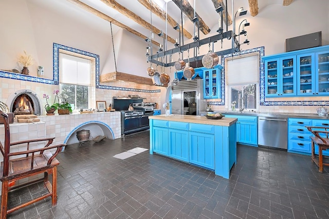 kitchen with beam ceiling, butcher block counters, stainless steel dishwasher, open floor plan, and blue cabinets