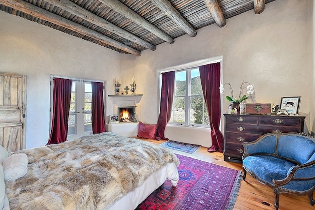 bedroom with beam ceiling, french doors, wood-type flooring, wood ceiling, and a lit fireplace