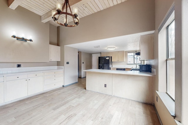 kitchen with black appliances, beamed ceiling, light countertops, and light wood-style flooring