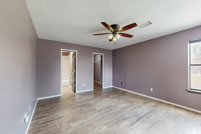 unfurnished bedroom with light wood-style floors, a walk in closet, visible vents, and baseboards