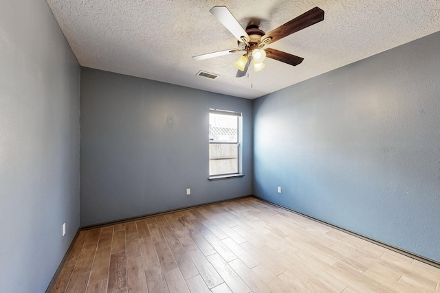 empty room featuring a textured ceiling, wood finished floors, visible vents, and a ceiling fan