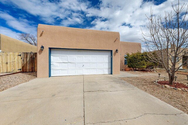 adobe home with a garage, driveway, fence, and stucco siding