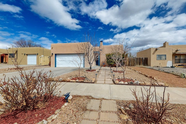 pueblo-style home with driveway, a garage, fence, and stucco siding