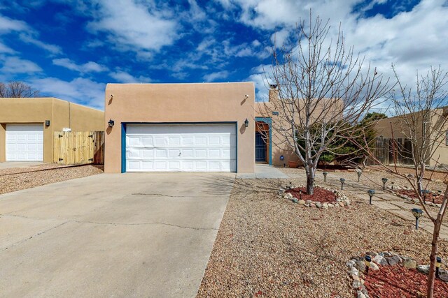 southwest-style home with an attached garage, fence, driveway, stucco siding, and a chimney