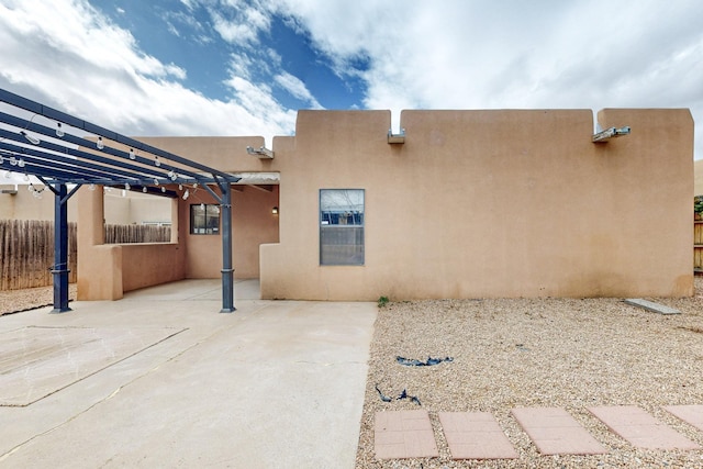 rear view of property featuring a pergola, stucco siding, a patio, and fence