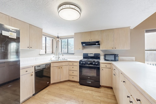 kitchen featuring light countertops, light brown cabinets, a sink, under cabinet range hood, and black appliances