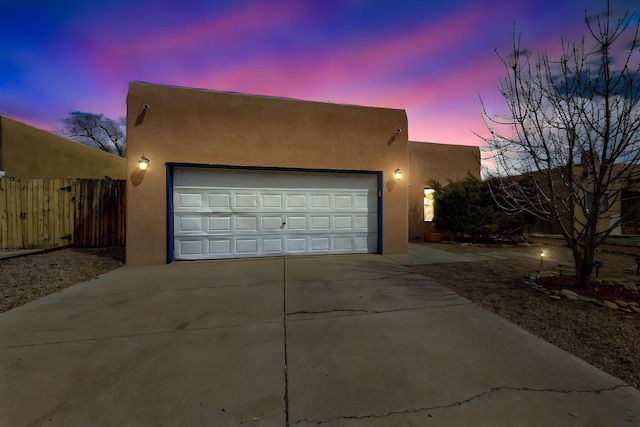 view of front of property featuring concrete driveway, an attached garage, fence, and stucco siding