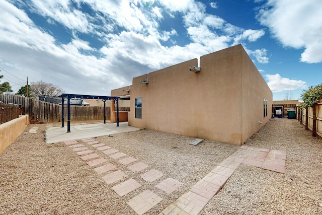 view of side of home featuring a patio area, a fenced backyard, a pergola, and stucco siding