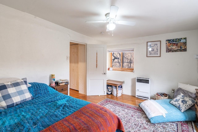 bedroom with ceiling fan, heating unit, and wood finished floors