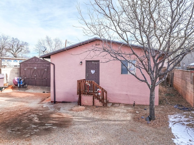 view of front of house with a shed, fence, an outbuilding, and stucco siding