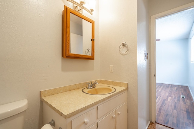 bathroom with toilet, baseboards, wood finished floors, and vanity