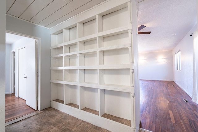 corridor featuring a textured ceiling, wood finished floors, visible vents, and baseboards