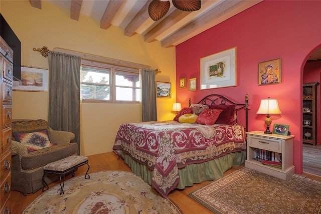 bedroom with arched walkways, beam ceiling, and wood finished floors