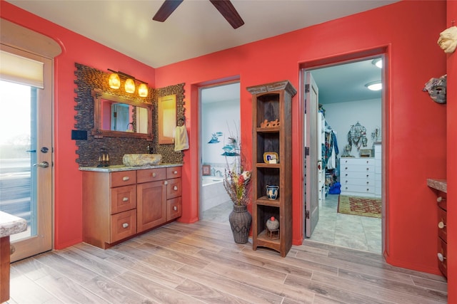 bathroom with wood finished floors, vanity, a ceiling fan, backsplash, and a bath