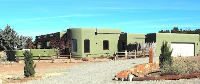 pueblo-style house with a garage, gravel driveway, fence, and stucco siding