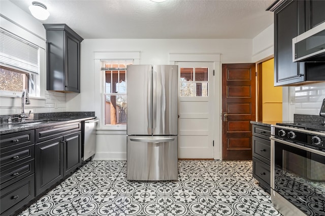 kitchen featuring decorative backsplash, dark stone counters, appliances with stainless steel finishes, dark cabinetry, and a sink