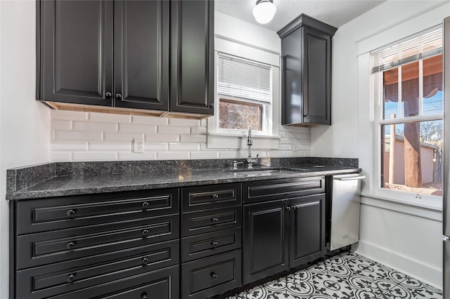 kitchen with stainless steel dishwasher, dark cabinetry, light tile patterned floors, a sink, and baseboards