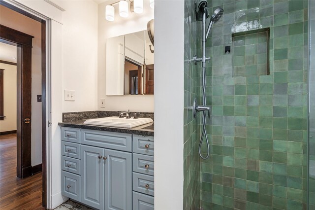 bathroom with a tile shower, wood finished floors, vanity, and baseboards