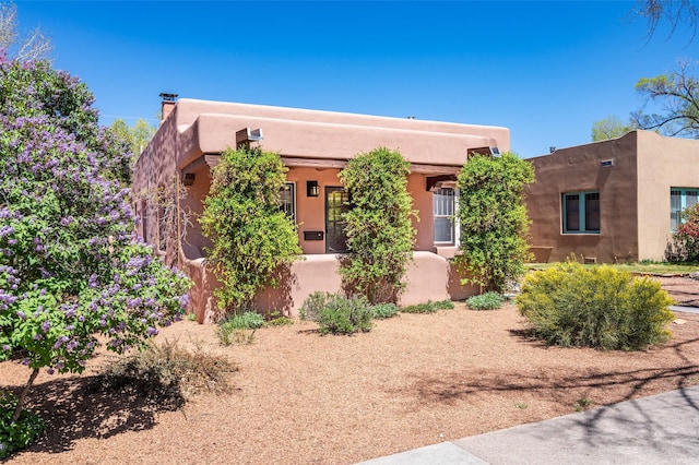 pueblo-style home featuring a chimney and stucco siding