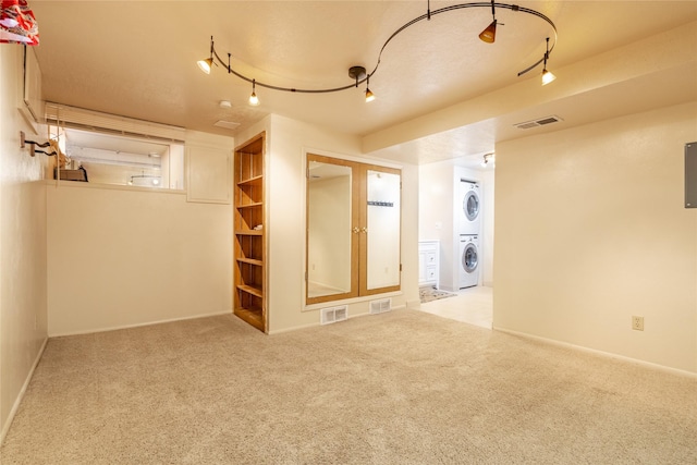unfurnished room featuring stacked washer / drying machine, carpet, rail lighting, and visible vents