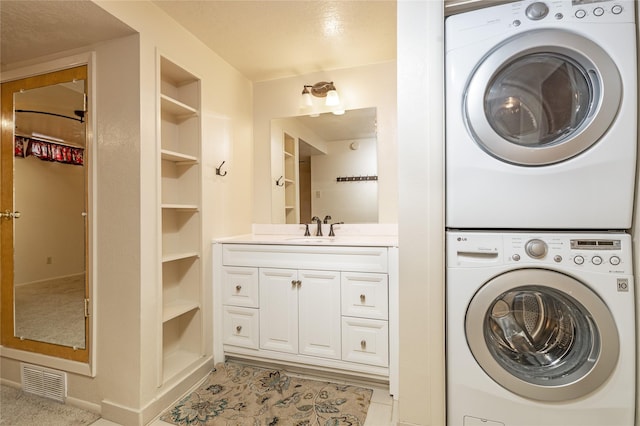 clothes washing area with a sink, laundry area, built in features, stacked washer / drying machine, and visible vents