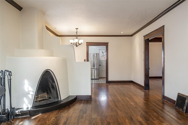 unfurnished living room featuring baseboards, a fireplace with raised hearth, hardwood / wood-style flooring, ornamental molding, and a chandelier