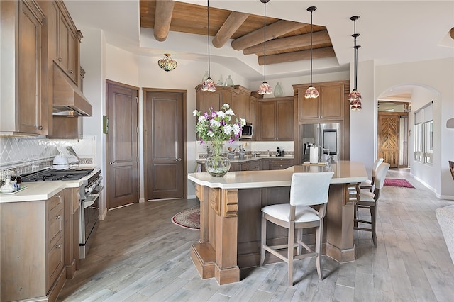 kitchen with backsplash, under cabinet range hood, wood ceiling, appliances with stainless steel finishes, and arched walkways