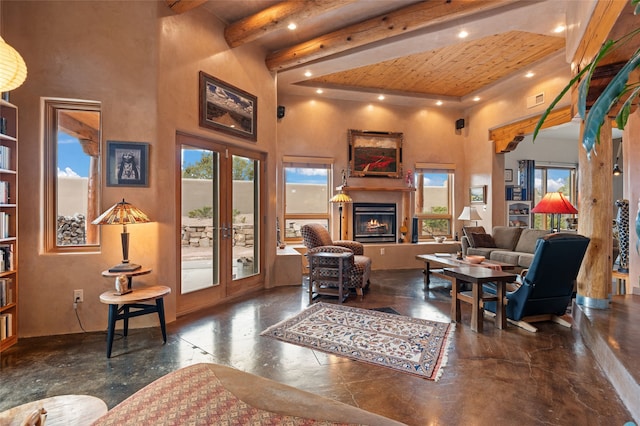 living room featuring a wealth of natural light, beamed ceiling, a high ceiling, and a lit fireplace