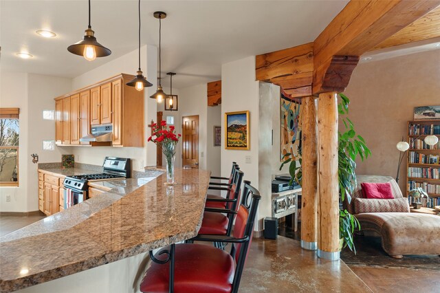 kitchen with finished concrete floors, hanging light fixtures, under cabinet range hood, stainless steel gas range oven, and a kitchen bar