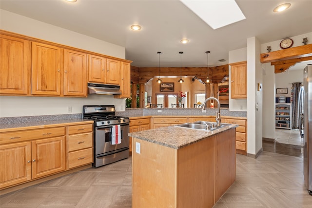 kitchen featuring stainless steel gas range oven, an island with sink, under cabinet range hood, a sink, and tile countertops