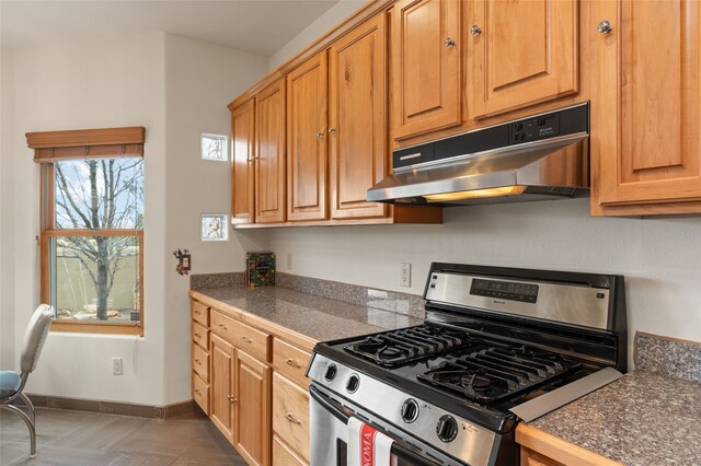 kitchen with stainless steel gas stove, tile countertops, baseboards, and under cabinet range hood