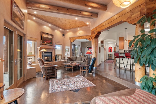 living room featuring beam ceiling, a high ceiling, recessed lighting, concrete flooring, and a glass covered fireplace