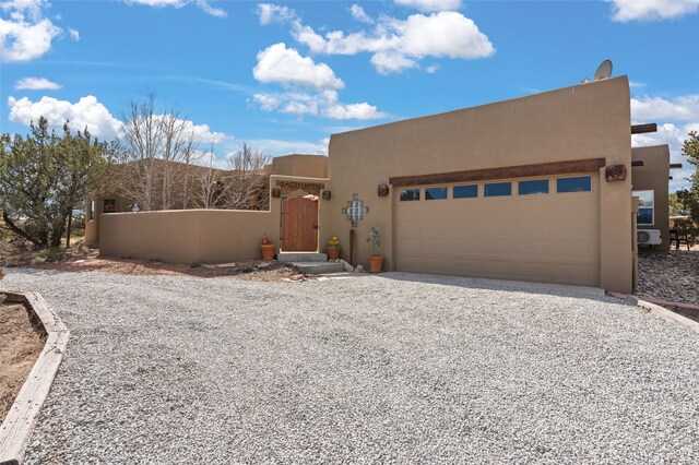 adobe home featuring gravel driveway, an attached garage, a fenced front yard, and stucco siding