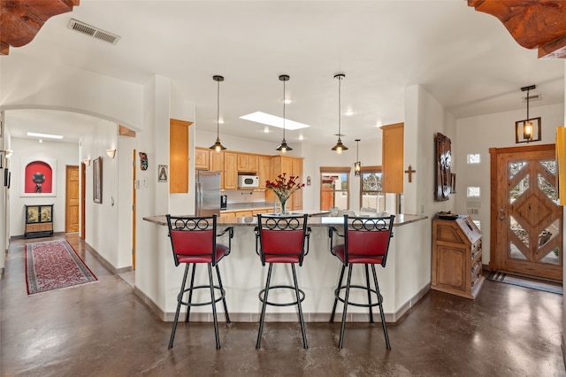 kitchen featuring white microwave, visible vents, concrete floors, a peninsula, and stainless steel fridge