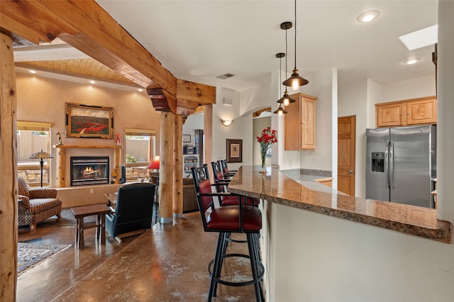 kitchen featuring stainless steel fridge with ice dispenser, finished concrete floors, open floor plan, decorative columns, and a glass covered fireplace