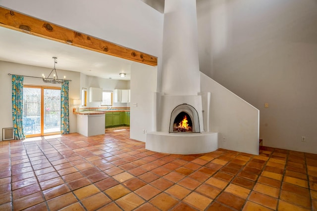 unfurnished living room featuring beamed ceiling, a lit fireplace, an inviting chandelier, and light tile patterned flooring