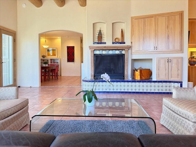 living area featuring arched walkways, a towering ceiling, a high end fireplace, and tile patterned flooring