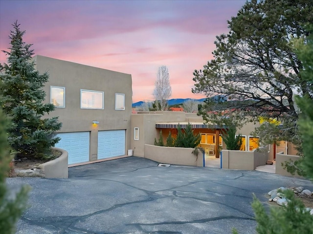 pueblo-style house with aphalt driveway, an attached garage, and stucco siding