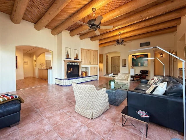 living area featuring light tile patterned floors, a ceiling fan, visible vents, a lit fireplace, and wooden ceiling