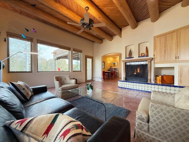 tiled living area with beamed ceiling, a ceiling fan, arched walkways, a lit fireplace, and wood ceiling