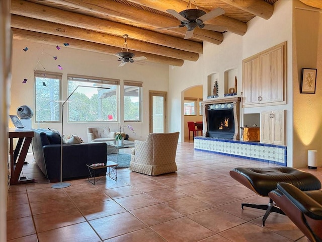 living area featuring tile patterned floors, beam ceiling, a warm lit fireplace, arched walkways, and wood ceiling