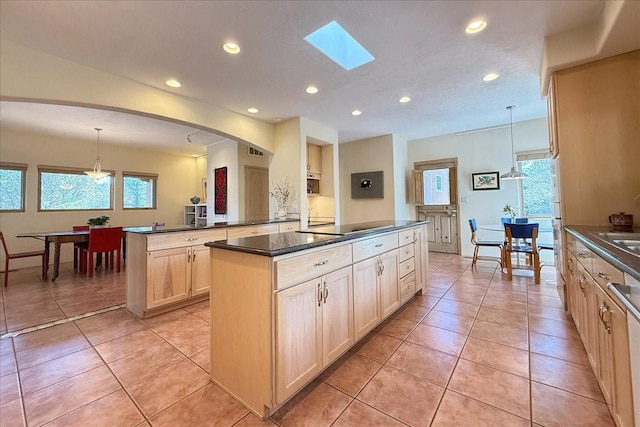 kitchen with light tile patterned floors, a kitchen island, dark countertops, and light brown cabinetry