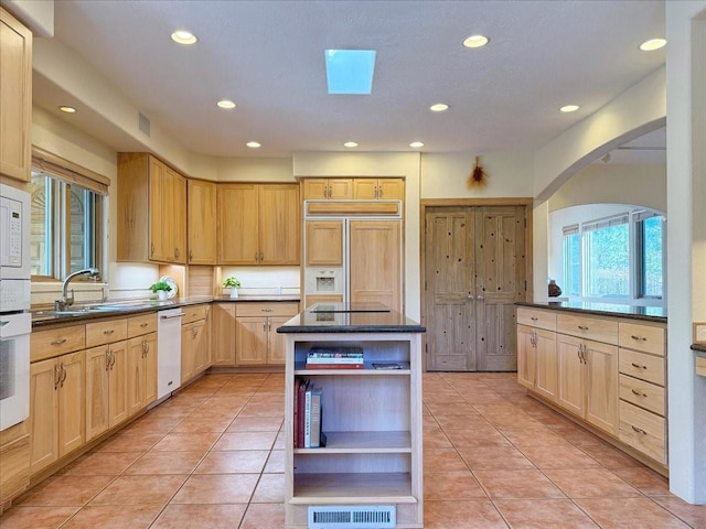 kitchen with paneled fridge, light brown cabinets, open shelves, a sink, and dark countertops