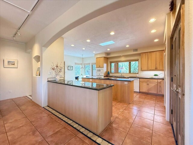 kitchen featuring dark countertops, white appliances, arched walkways, a peninsula, and light tile patterned flooring