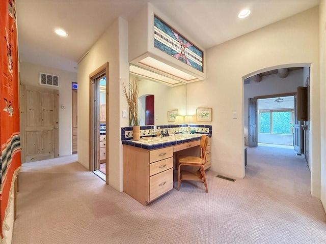 interior space featuring arched walkways, visible vents, light carpet, and tile counters