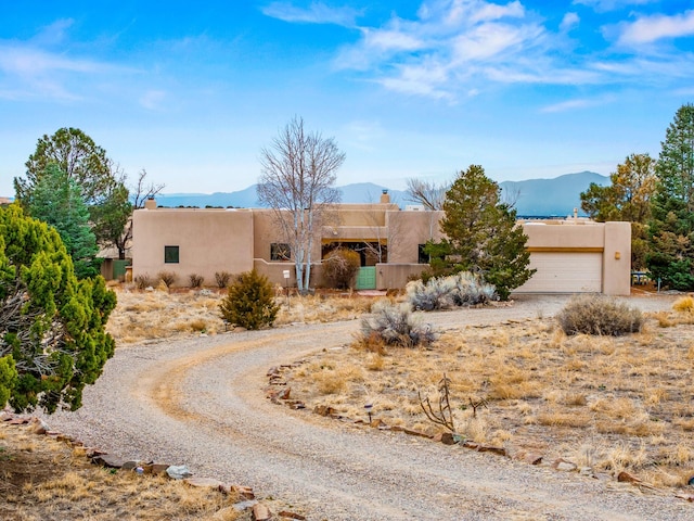 pueblo-style home featuring stucco siding, a mountain view, and an attached garage